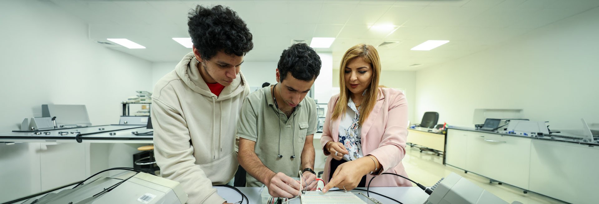 A female instructor and two male students working together on an electronics project in a bright engineering lab